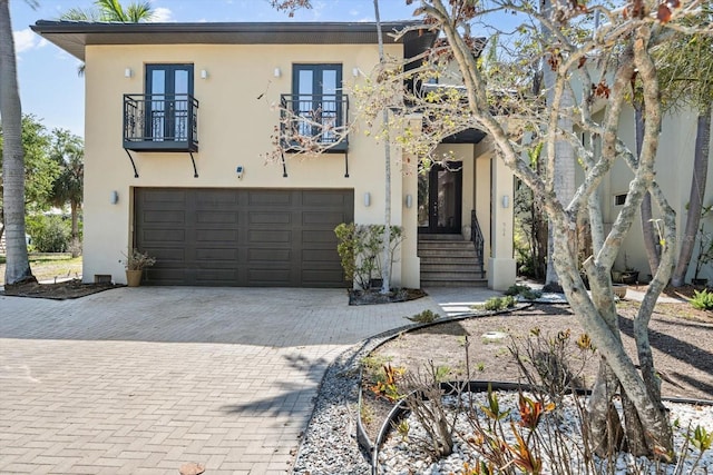 view of front of house featuring an attached garage, a balcony, french doors, stucco siding, and driveway