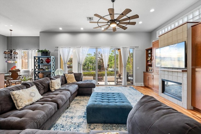 living area with light wood-type flooring, recessed lighting, visible vents, a tile fireplace, and ceiling fan with notable chandelier