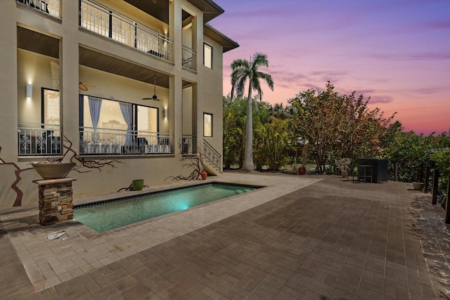 pool at dusk featuring an outdoor pool, a patio, and ceiling fan