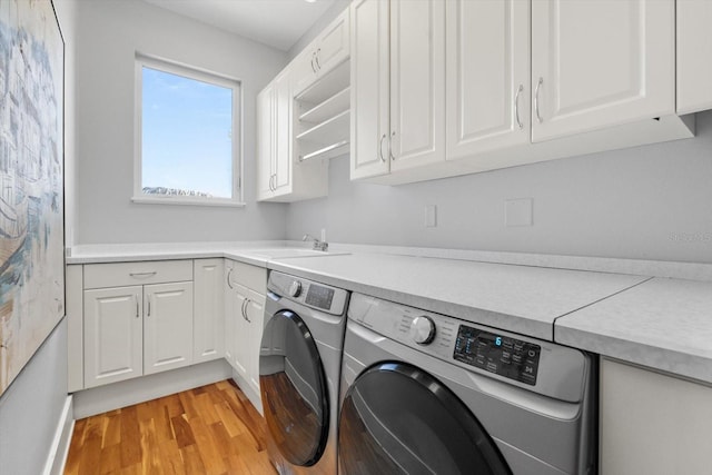 laundry room with cabinet space, washing machine and clothes dryer, a sink, and light wood-style flooring