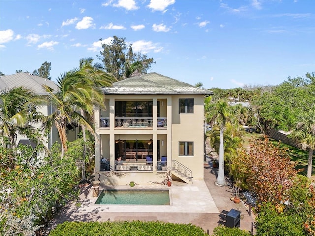 rear view of property featuring a patio area, an outdoor pool, a balcony, and stucco siding