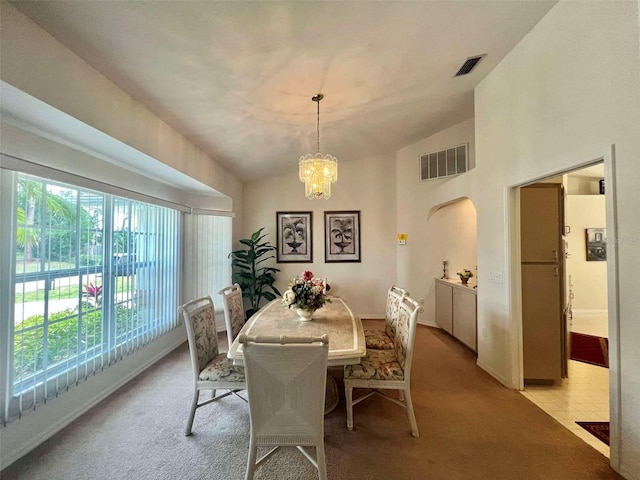dining area featuring light carpet, lofted ceiling, a chandelier, and visible vents