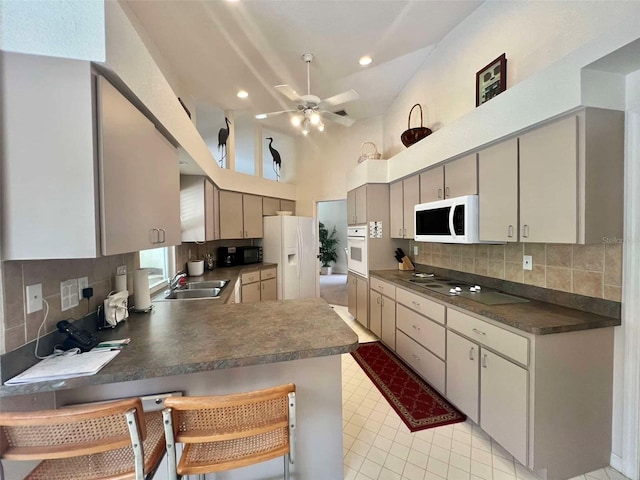 kitchen featuring white appliances, a sink, dark countertops, ceiling fan, and a peninsula