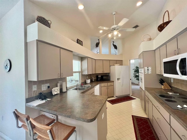 kitchen featuring a sink, a peninsula, white appliances, dark countertops, and ceiling fan