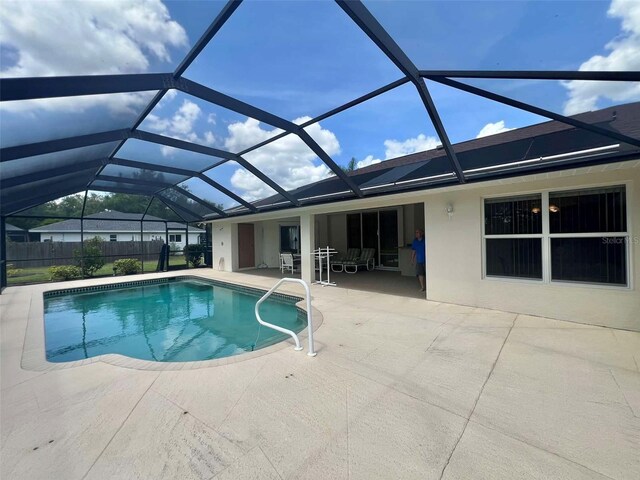 outdoor pool with glass enclosure, fence, and a patio area