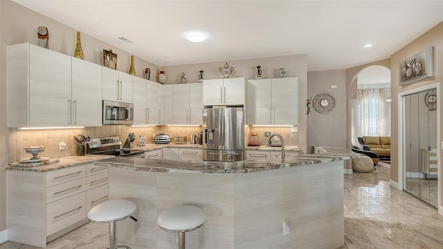 1085 Mallard Marsh Dr, Osprey, FL 34229 - kitchen with light stone countertops, decorative backsplash, arched walkways, and appliances with stainless steel finishes