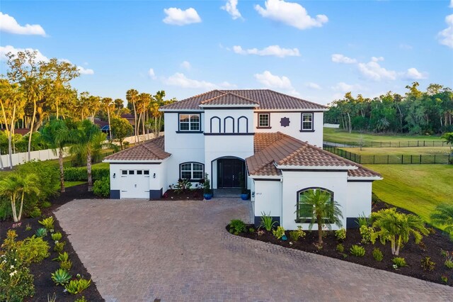 mediterranean / spanish house featuring fence, decorative driveway, stucco siding, a tiled roof, and an attached garage
