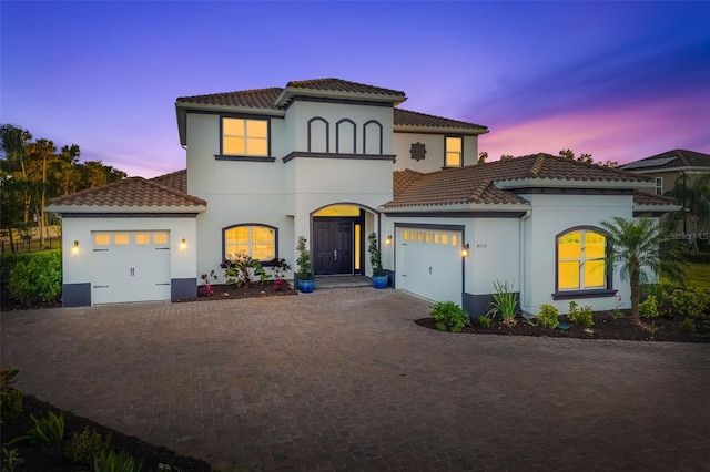 mediterranean / spanish house featuring an attached garage, decorative driveway, and a tiled roof