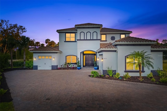 mediterranean / spanish-style home with stucco siding, decorative driveway, a tile roof, and a garage