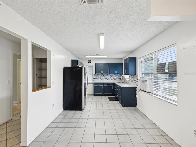 kitchen featuring blue cabinets, freestanding refrigerator, a sink, and light tile patterned floors