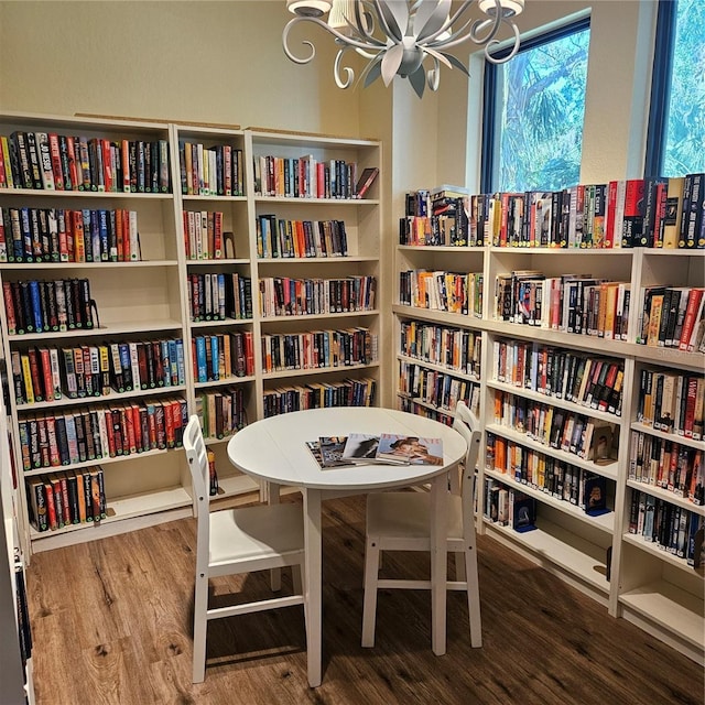 sitting room with wall of books, a chandelier, and wood finished floors