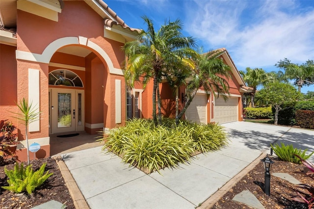entrance to property featuring an attached garage, concrete driveway, and stucco siding