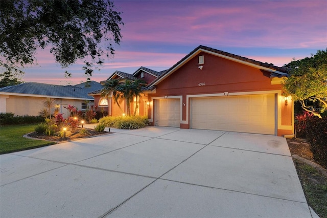 view of front of house with an attached garage, a tiled roof, concrete driveway, and stucco siding