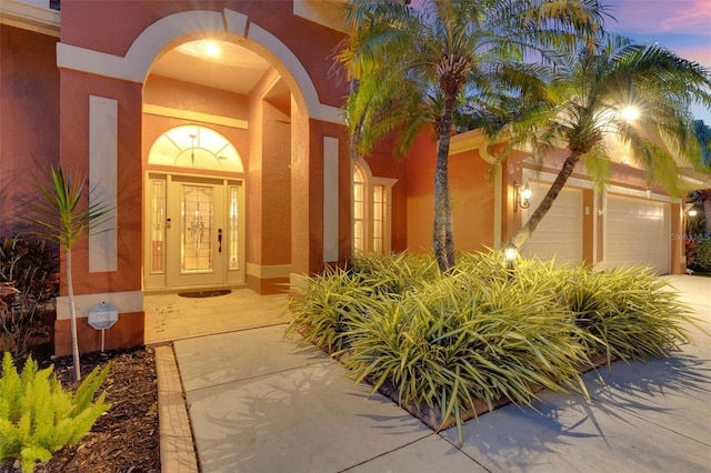 entrance to property featuring a garage, stucco siding, and concrete driveway