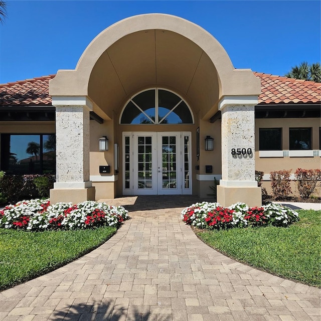 view of exterior entry with french doors, stucco siding, and a tiled roof