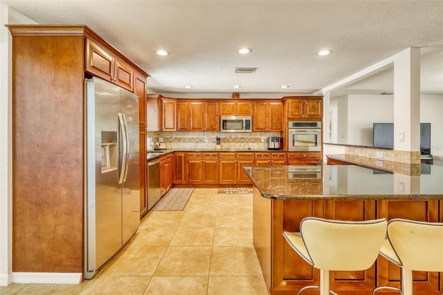 2605 Sunnybrook Dr, Sarasota, FL 34239 - kitchen featuring a breakfast bar area, brown cabinetry, appliances with stainless steel finishes, tasteful backsplash, and dark stone counters