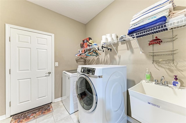laundry area featuring light tile patterned flooring, a textured ceiling, laundry area, a sink, and washer and dryer