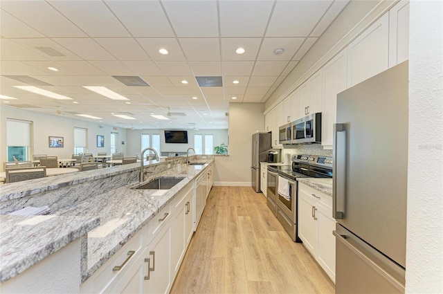 kitchen with white cabinetry, open floor plan, a sink, and appliances with stainless steel finishes