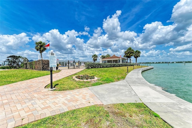 view of community with a gate, a water view, fence, and a lawn
