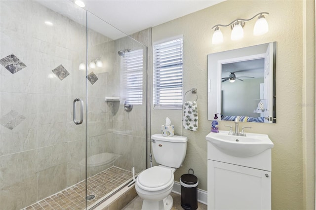 bathroom featuring a stall shower, toilet, vanity, baseboards, and ceiling fan