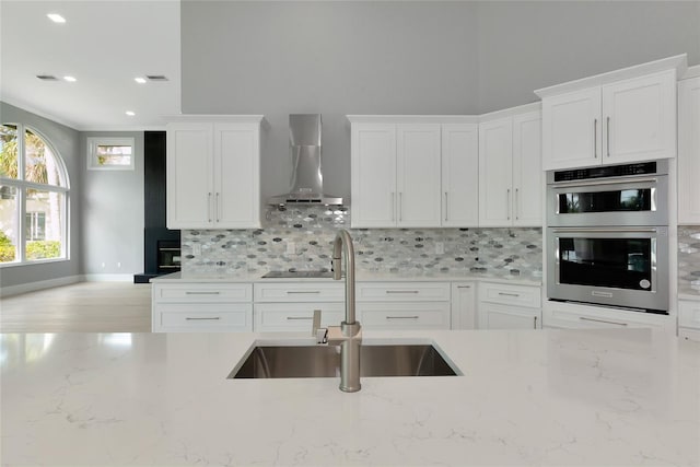 600 Eagle Watch Ln, Osprey, FL 34229 - kitchen featuring wall chimney range hood, stainless steel double oven, decorative backsplash, white cabinets, and light stone counters