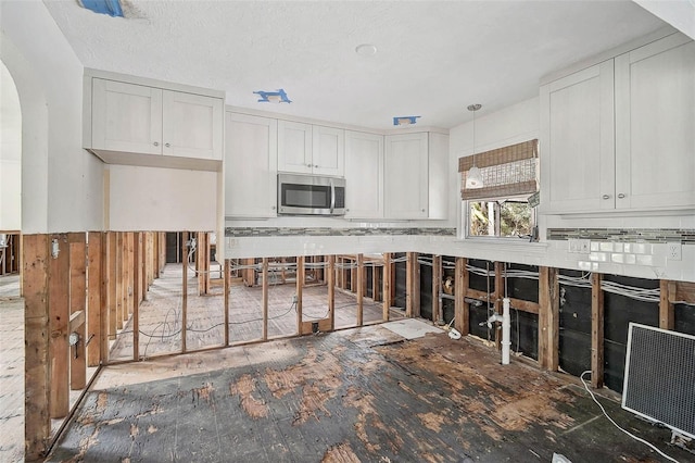 kitchen featuring stainless steel microwave, arched walkways, and white cabinetry