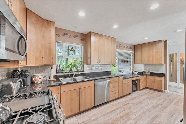 kitchen with dark countertops, tasteful backsplash, a sink, light wood-style floors, and stainless steel appliances