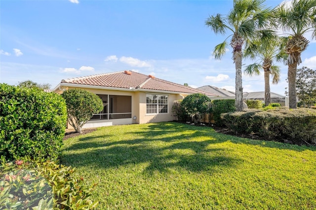 back of property featuring a tile roof, a sunroom, a lawn, and stucco siding