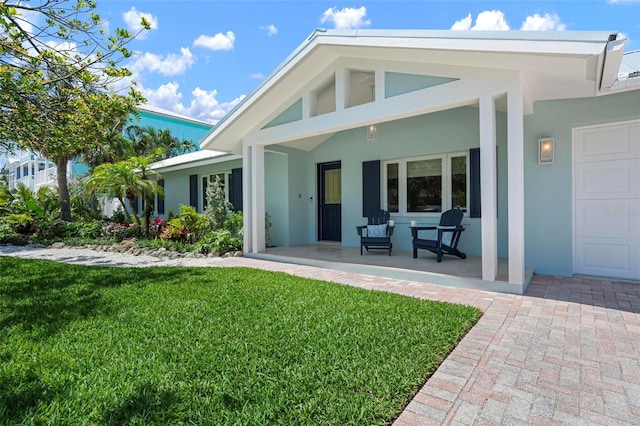 back of property with a yard, covered porch, and stucco siding