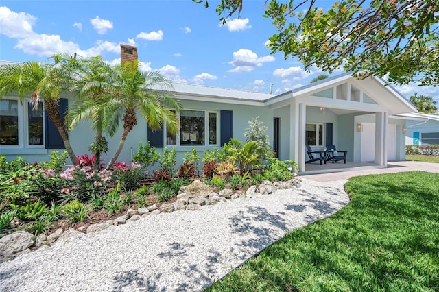 single story home with metal roof, a garage, a chimney, stucco siding, and a front lawn