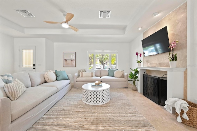 living area with visible vents, a tray ceiling, a ceiling fan, and a premium fireplace