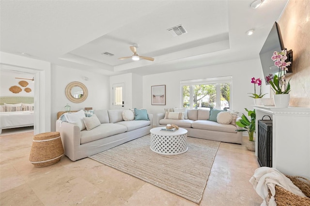 living area featuring a raised ceiling, ceiling fan, a fireplace, and visible vents