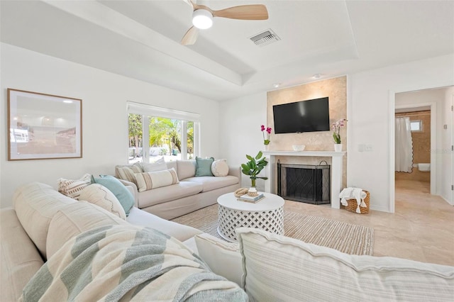 living room with baseboards, a fireplace, a raised ceiling, visible vents, and ceiling fan
