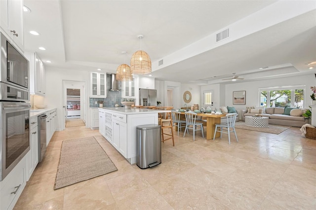 kitchen featuring wall chimney range hood, visible vents, appliances with stainless steel finishes, and a raised ceiling