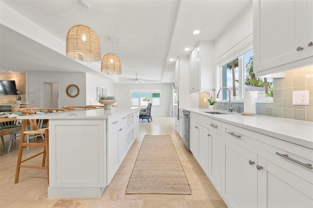 kitchen with light countertops, a kitchen island, decorative backsplash, dishwasher, and a sink