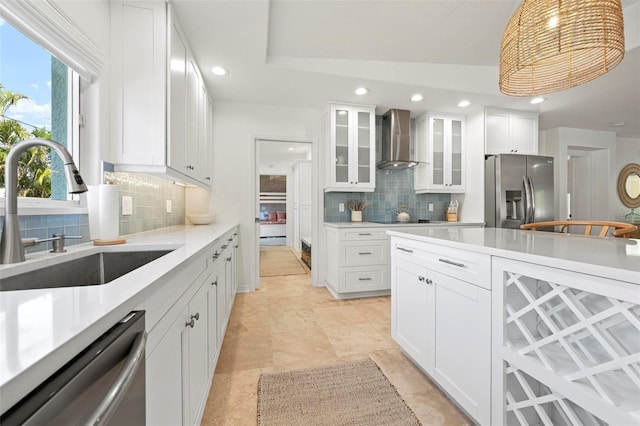 kitchen featuring white cabinets, wall chimney exhaust hood, a sink, stainless steel appliances, and decorative backsplash
