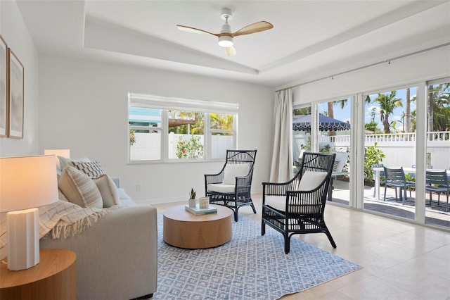 living area featuring a raised ceiling and ceiling fan