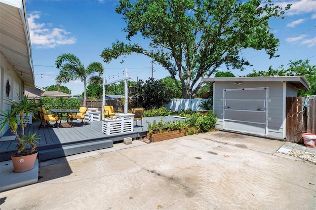 view of patio / terrace featuring a deck, an outbuilding, a storage unit, and fence