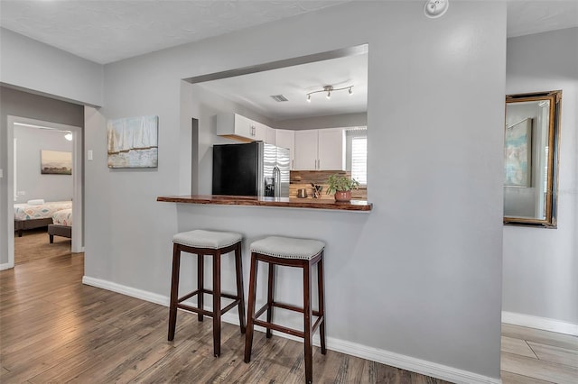 kitchen with white cabinetry, stainless steel fridge, wood finished floors, and a breakfast bar area