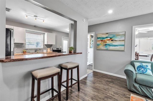 kitchen with tasteful backsplash, white cabinets, appliances with stainless steel finishes, a breakfast bar, and dark wood finished floors