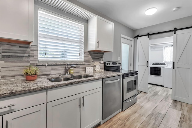 kitchen with appliances with stainless steel finishes, washing machine and dryer, white cabinetry, decorative backsplash, and a sink