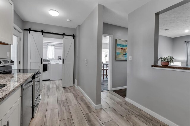 kitchen featuring light stone countertops, a barn door, appliances with stainless steel finishes, wood tiled floor, and washer and clothes dryer