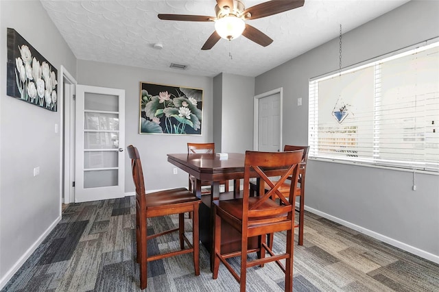 carpeted dining space with visible vents, baseboards, a ceiling fan, and a textured ceiling