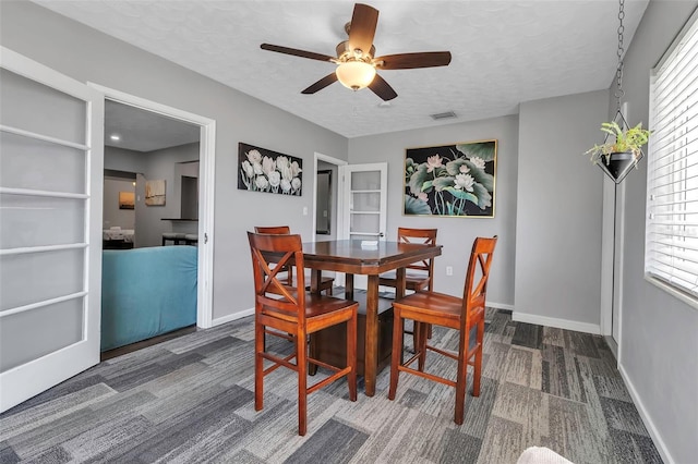 dining space featuring visible vents, baseboards, dark carpet, a ceiling fan, and a textured ceiling
