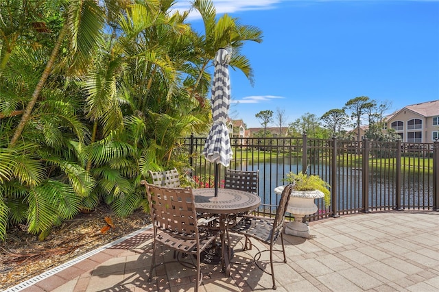 view of patio featuring a water view, outdoor dining space, and fence