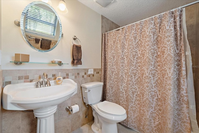 full bath with curtained shower, toilet, tile walls, a textured ceiling, and a wainscoted wall