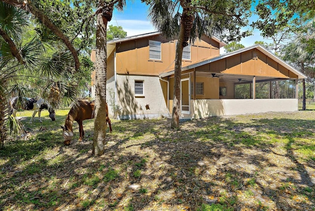 rear view of house featuring a sunroom, stucco siding, and a ceiling fan