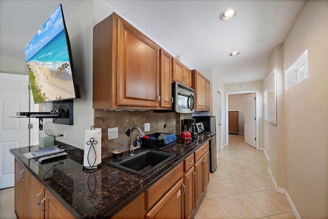 kitchen with stainless steel microwave, tasteful backsplash, light tile patterned floors, brown cabinets, and a sink