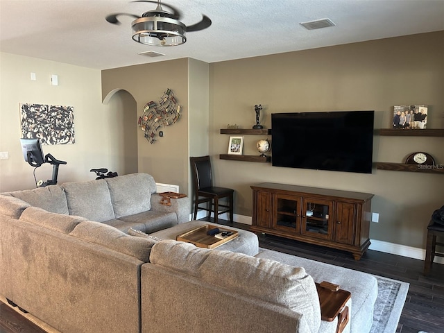living area featuring dark wood finished floors, visible vents, baseboards, and arched walkways
