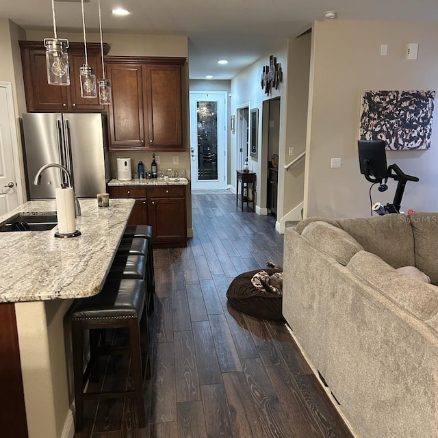 kitchen featuring freestanding refrigerator, a sink, a kitchen breakfast bar, open floor plan, and dark wood-style floors